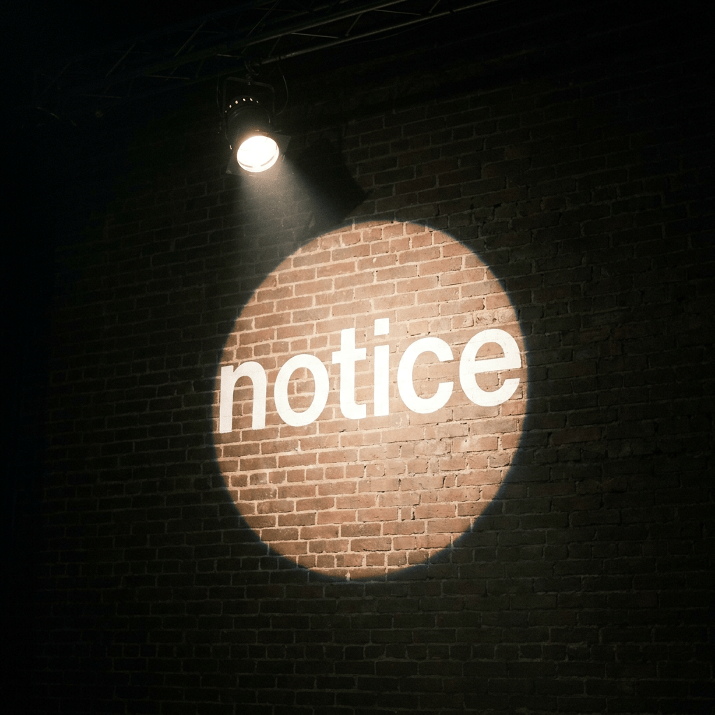 The word 'notice' illuminated by a spotlight on a brick wall